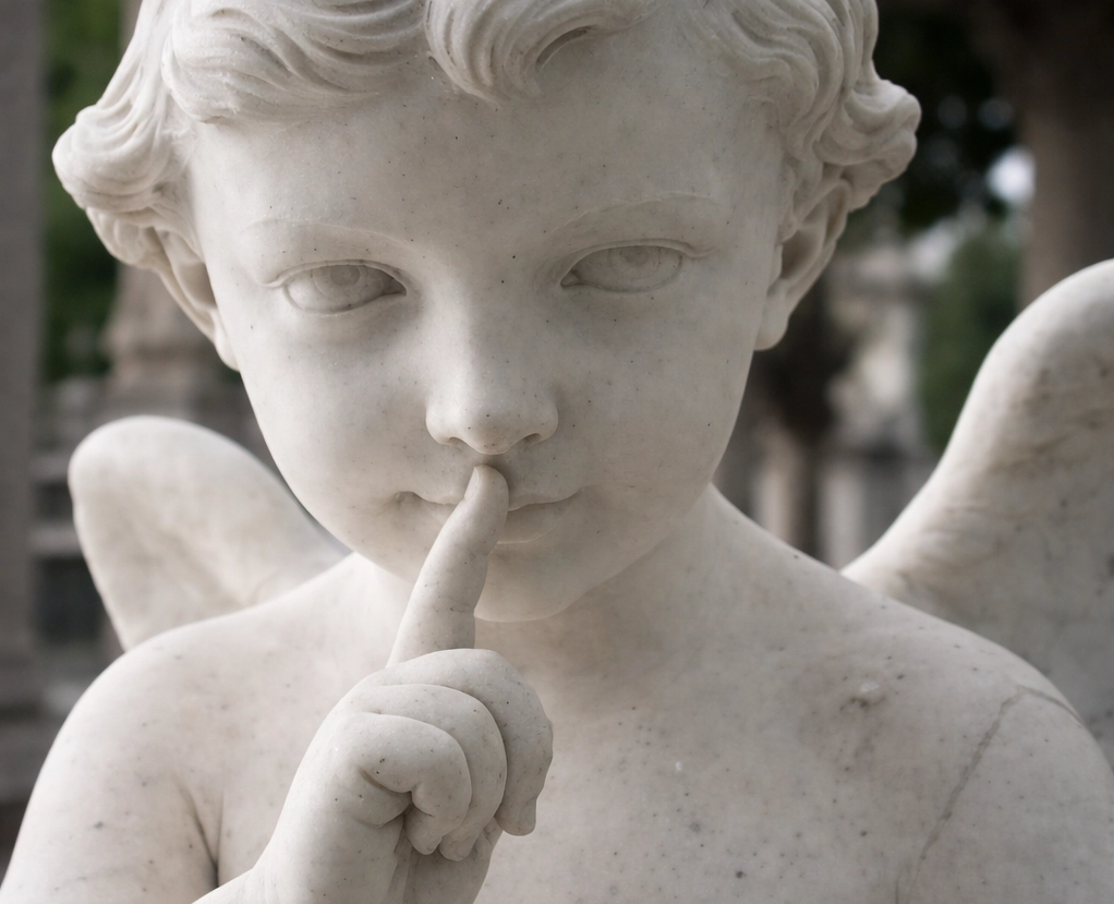 Estatua de ángel haciendo el gesto del silencio con el dedo sobre los labios, símbolo del misterio del filtrum y el conocimiento olvidado antes de nacer.